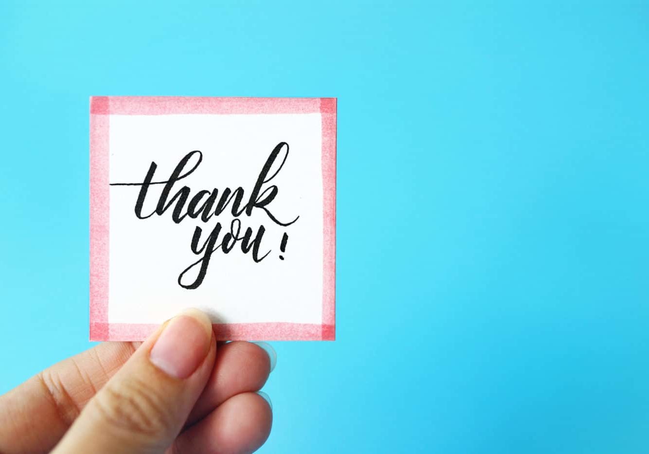 Cropped Hand Holding Thank You Text Against Blue Background